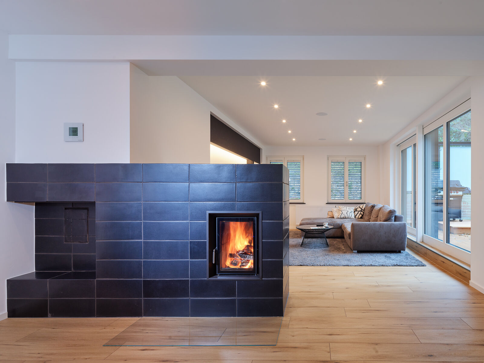 Schwarzer Tunnel Kachelofen als Raumteiler mit Blick auf ein modernes Wohnzimmer