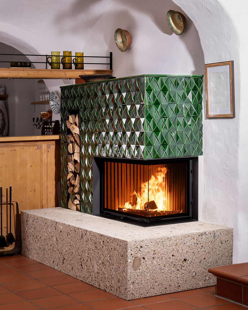 Eckkamin mit grüner Kachel und Steinsockel in einem Gewölbekeller