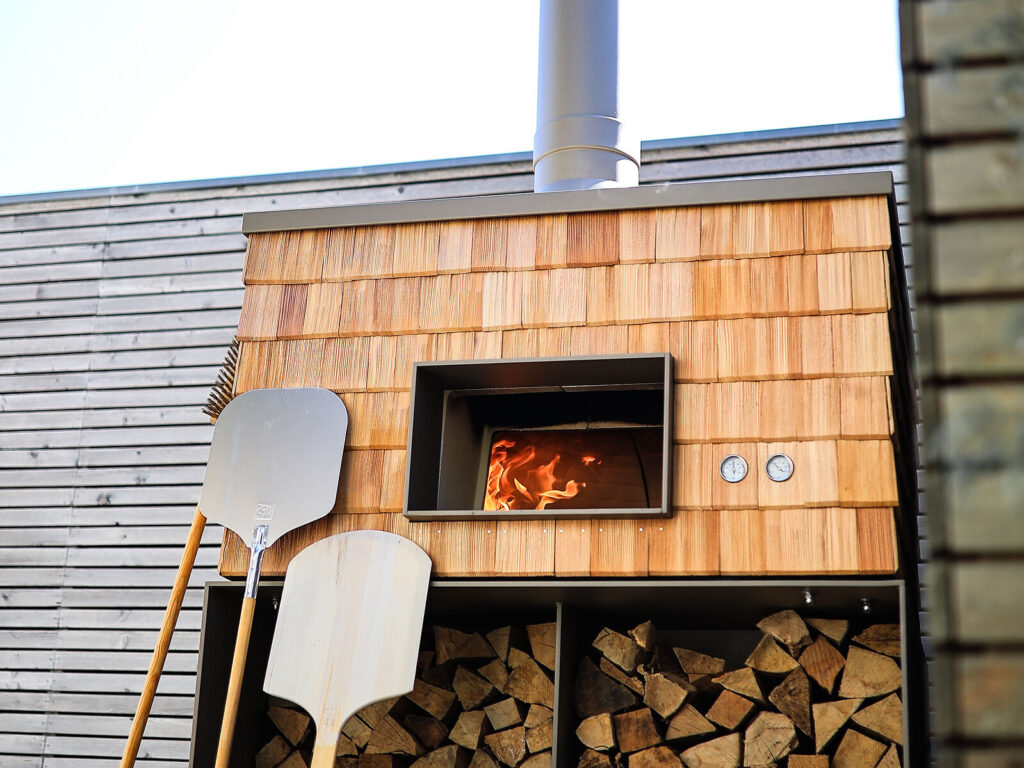Moderner Pizzaofen Feueriglu mit Holzverkleidung und Holzlege