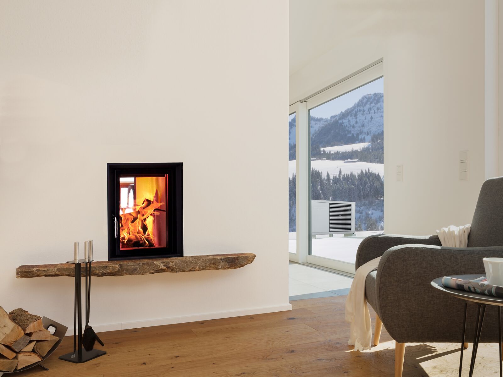 Kachelofen in Wohnraum, vor dem Fenster steht eine Wärmepumpe