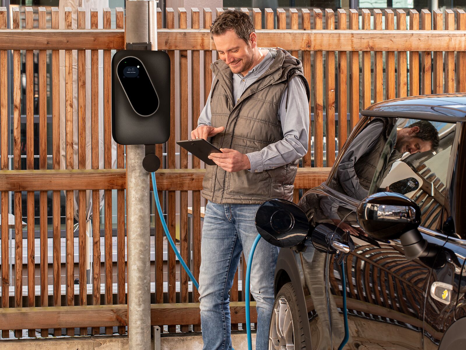 Mann stellt die Wallbox mit seinem Tablet zum Laden seines Autos ein
