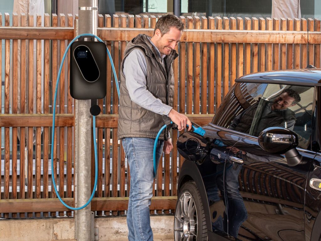 Mann steckt das Ladekabel der Wallbox an seinem Auto an
